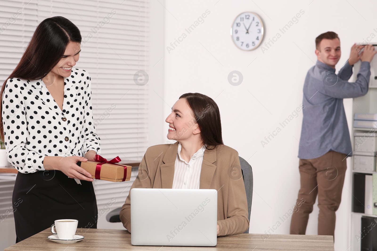 Photo of Woman presenting gift to her colleague in office