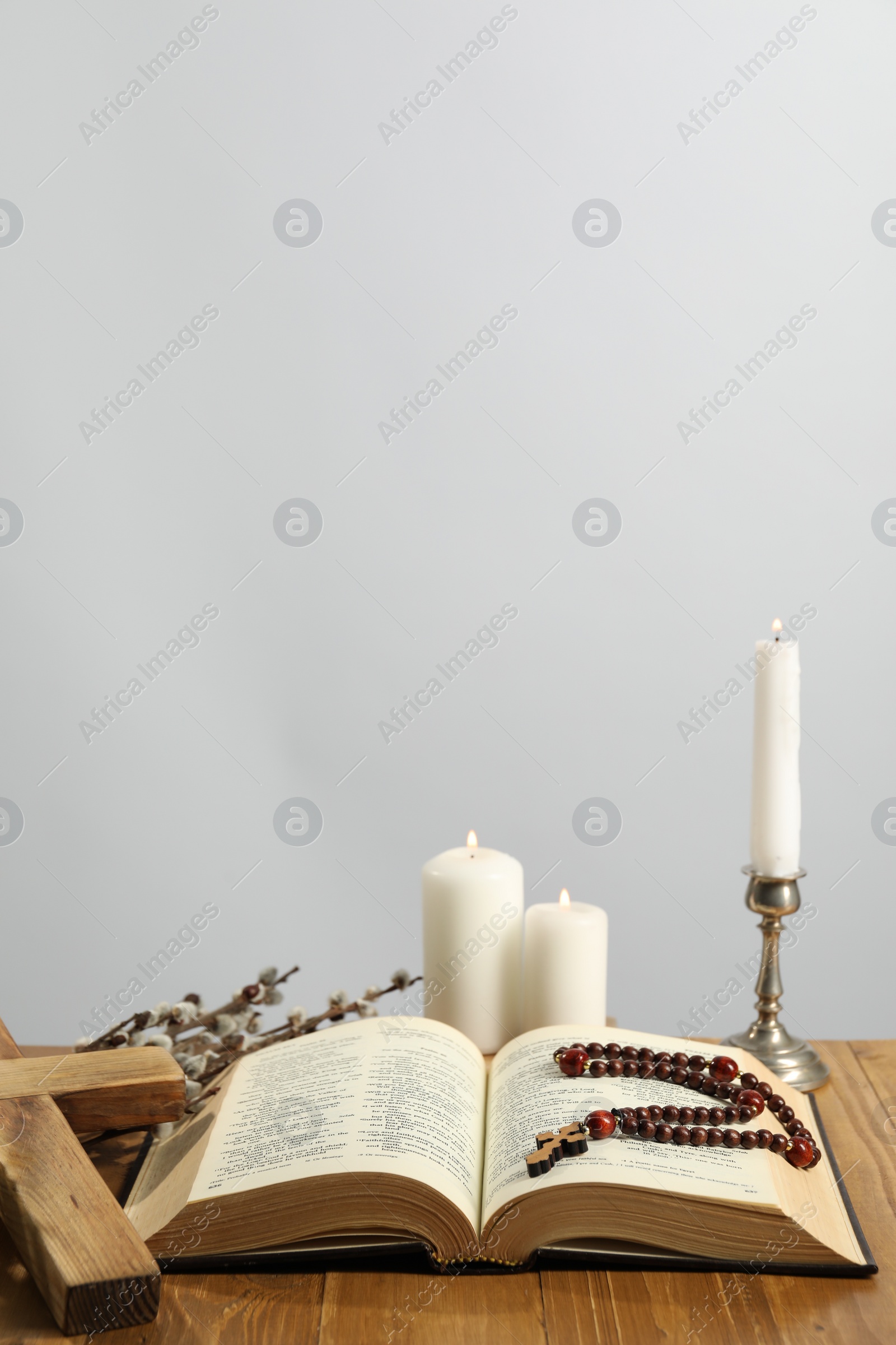 Photo of Church candles, cross, rosary beads, Bible and willow branches on wooden table against light background. Space for text