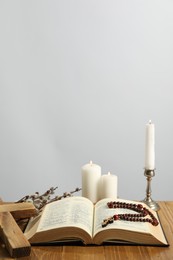 Photo of Church candles, cross, rosary beads, Bible and willow branches on wooden table against light background. Space for text