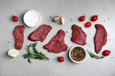 Photo of Fresh raw meat steaks and spices on light grey table, flat lay