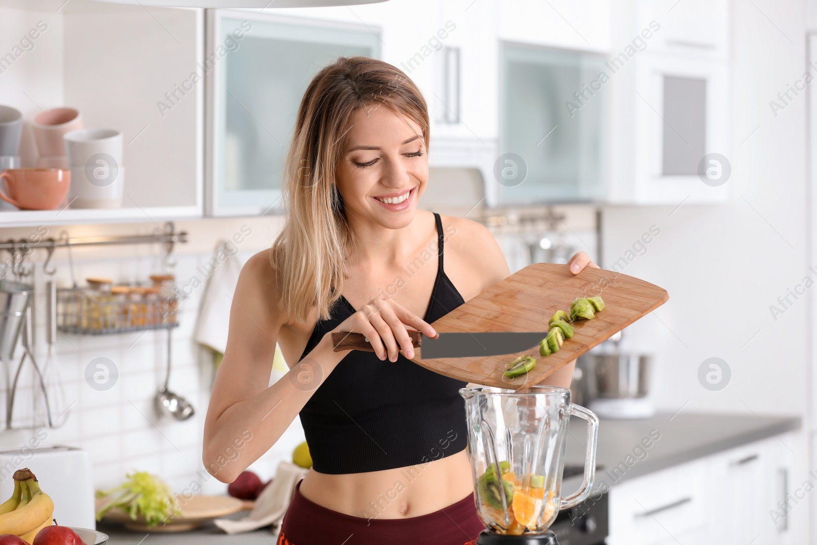 Photo of Young woman preparing tasty healthy smoothie in kitchen