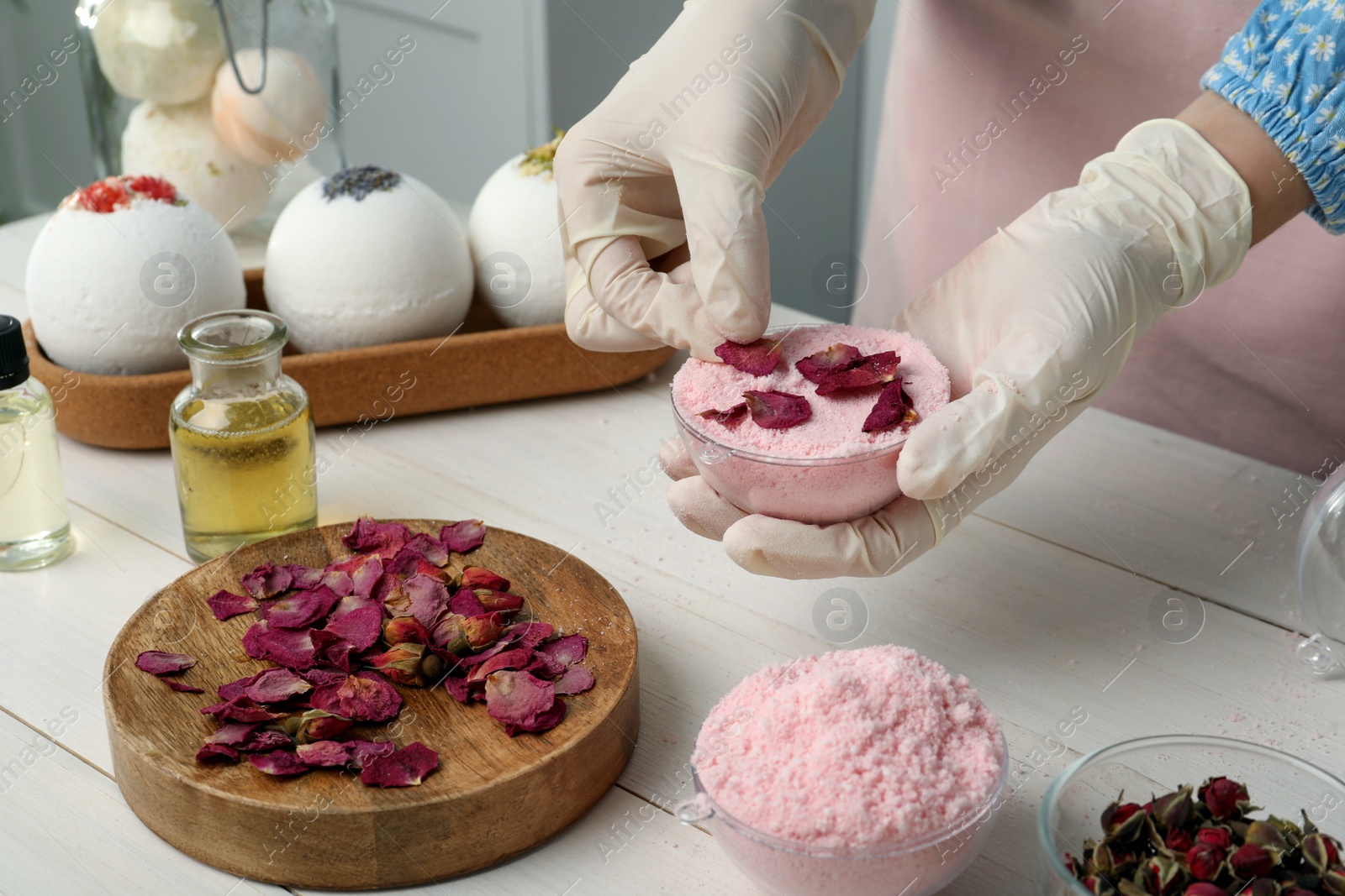 Photo of Woman in gloves making bath bomb at white table indoors, closeup