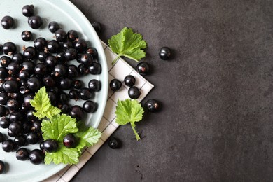 Photo of Plate with ripe blackcurrants and leaves on grey background, flat lay. Space for text