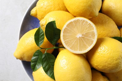 Fresh lemons and green leaves on light table, top view