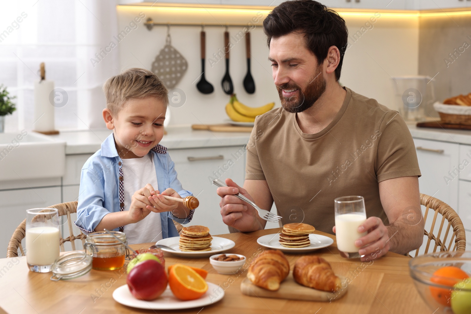 Photo of Father and his cute little son having breakfast at table in kitchen