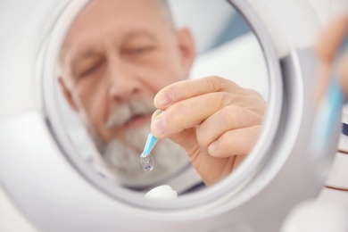 Mirror reflection of senior man taking contact lens from container