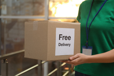 Photo of Courier holding parcel with sticker Free Delivery indoors, closeup