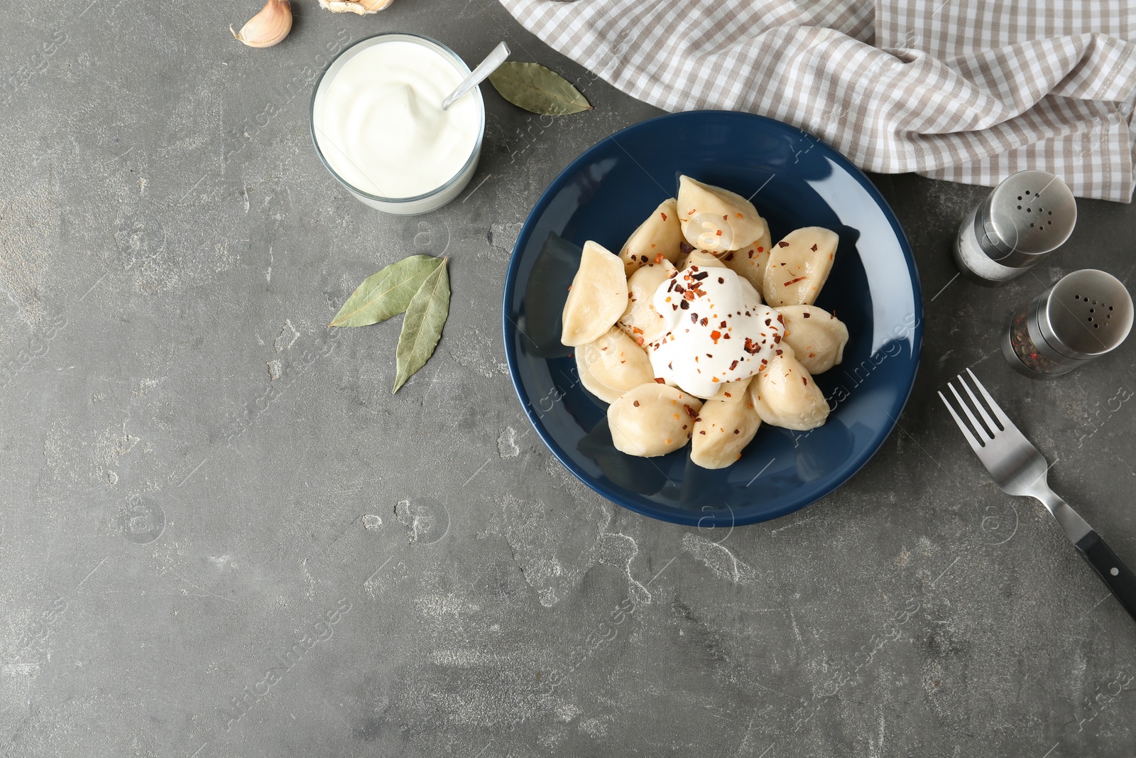 Photo of Delicious cooked dumplings with sour cream on grey table, flat lay. Space for text