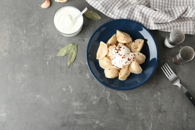 Delicious cooked dumplings with sour cream on grey table, flat lay. Space for text