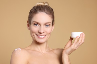 Woman with jar of body cream on beige background