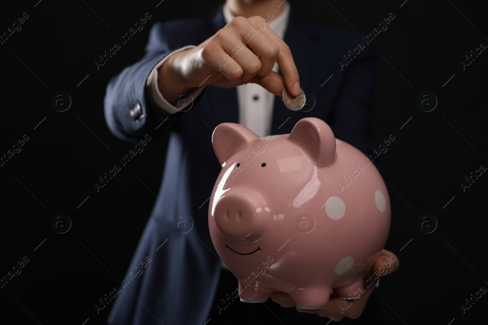 Photo of Woman putting coin into piggy bank on black background, closeup