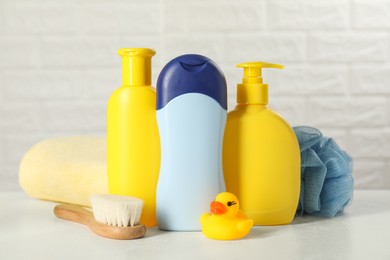 Photo of Baby cosmetic products, bath duck, brush and towel on white table against brick wall