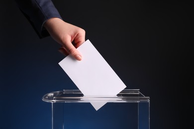 Photo of Woman putting her vote into ballot box on dark blue background, closeup