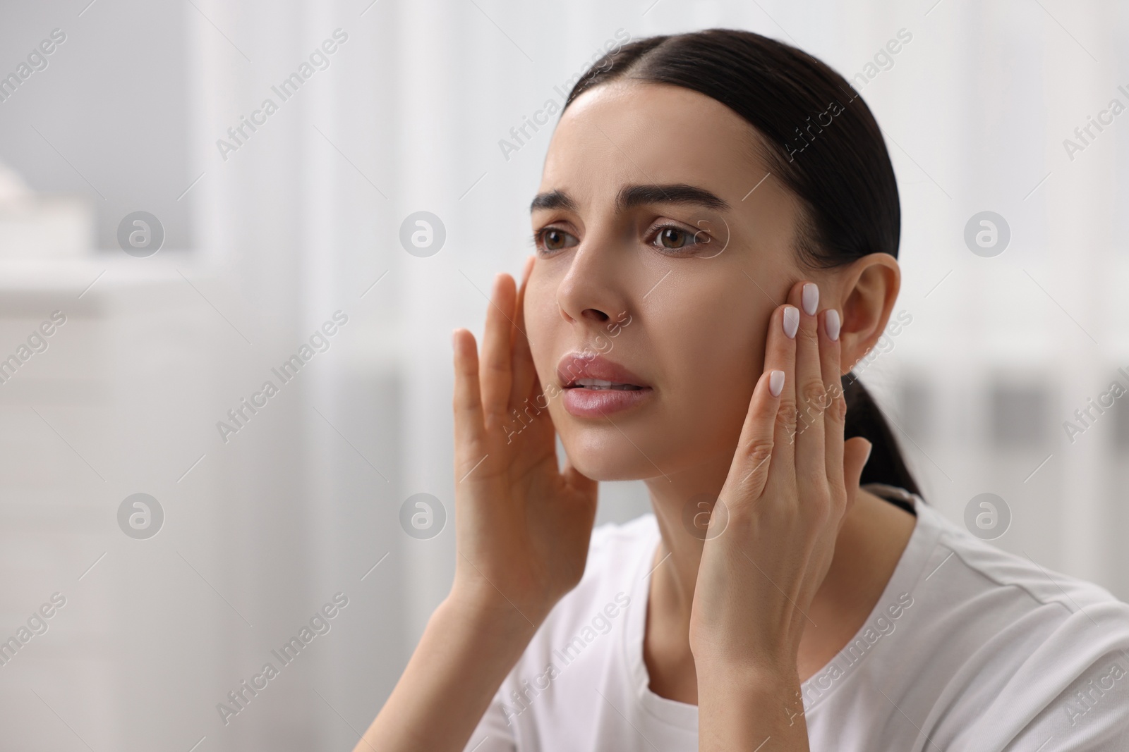 Photo of Woman with dry skin checking her face indoors, space for text