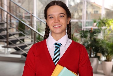Photo of Teenage girl in school uniform with books indoors