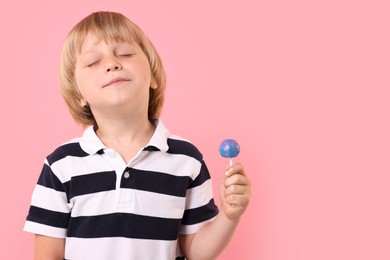 Cute little boy with lollipop on pink background, space for text