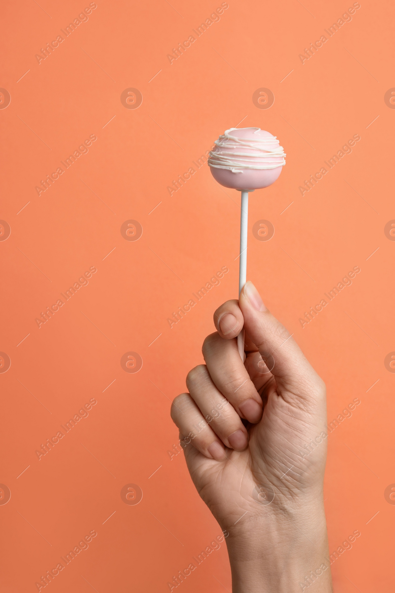 Photo of Woman holding sweet cake pop on coral background, closeup