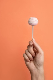 Woman holding sweet cake pop on coral background, closeup