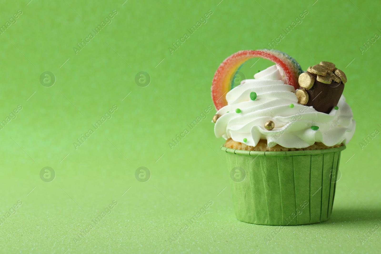 Photo of St. Patrick's day party. Tasty cupcake with sour rainbow belt and pot of gold toppers on green background. Space for text