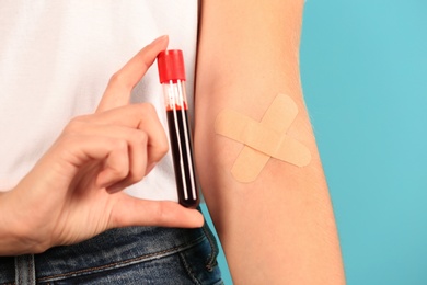 Woman holding test tube near hand with adhesive plasters against color background, closeup. Blood donation