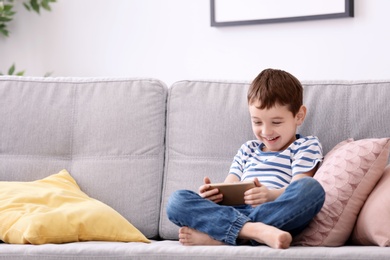 Photo of Cute little boy with mobile phone on sofa at home