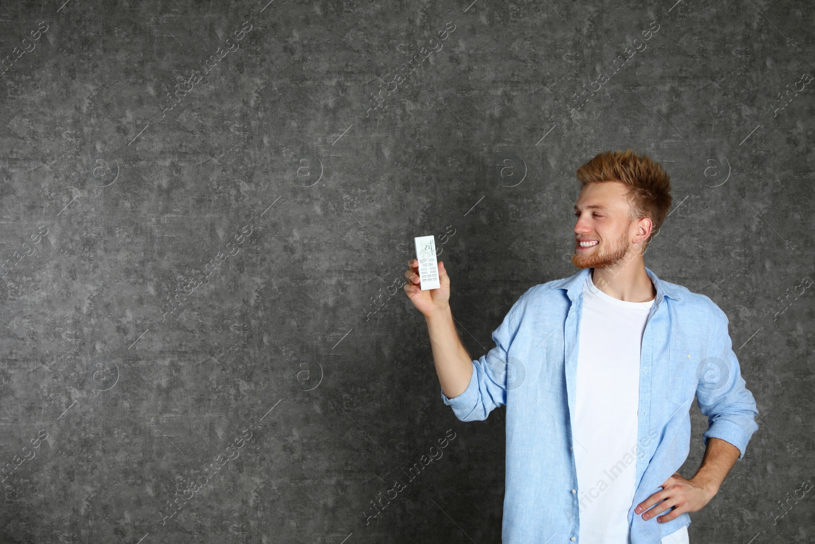 Photo of Young man with air conditioner remote on grey background. Space for text