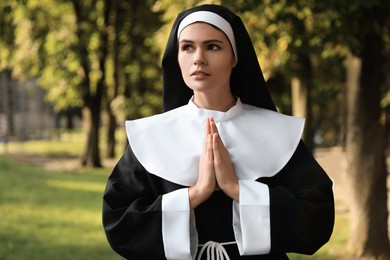 Photo of Young nun with hands clasped together praying in park