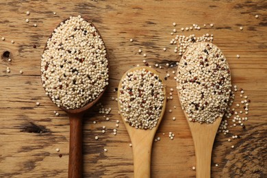 Photo of Spoons with raw quinoa seeds on wooden table, flat lay