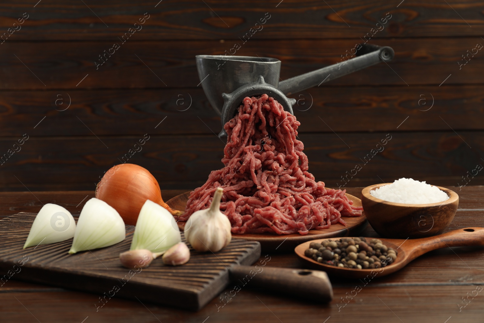 Photo of Meat grinder with beef mince, onion, garlic and spices on wooden table