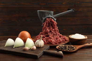Meat grinder with beef mince, onion, garlic and spices on wooden table