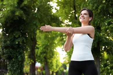 Photo of Young woman with wireless earphones doing morning exercise outdoors