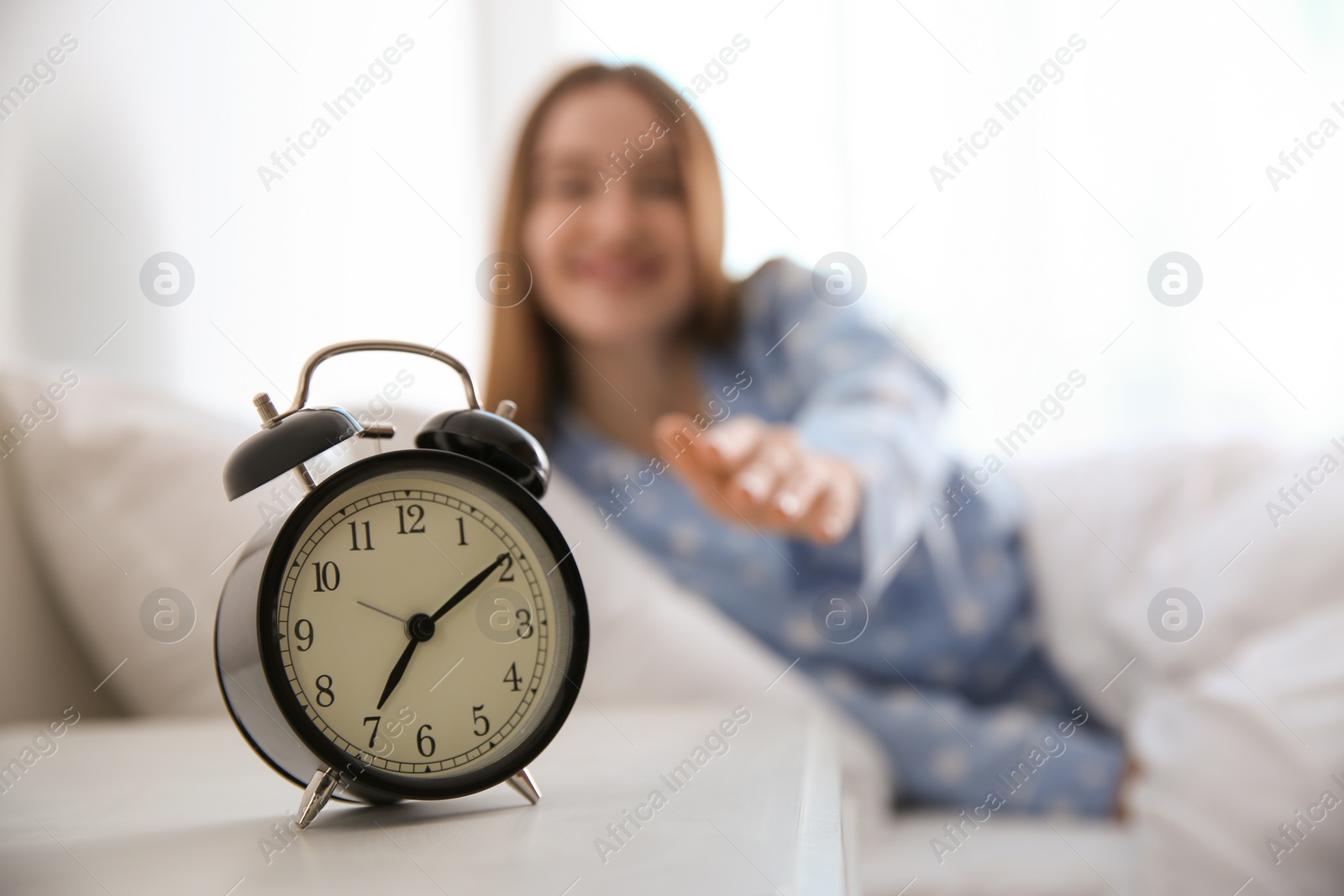 Photo of Young woman at home in morning, focus on alarm clock