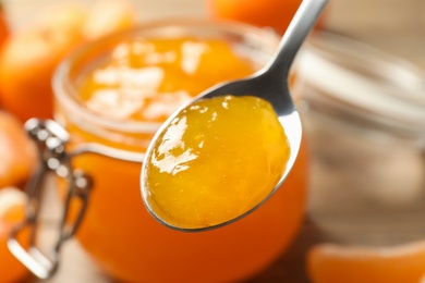 Photo of Teaspoon with tasty tangerine jam over table, closeup