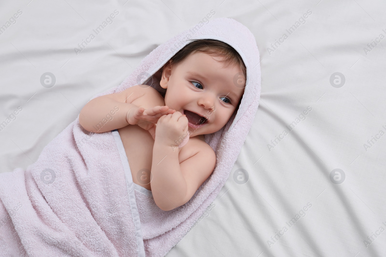 Photo of Cute little baby with pacifier in hooded towel after bathing on bed, top view