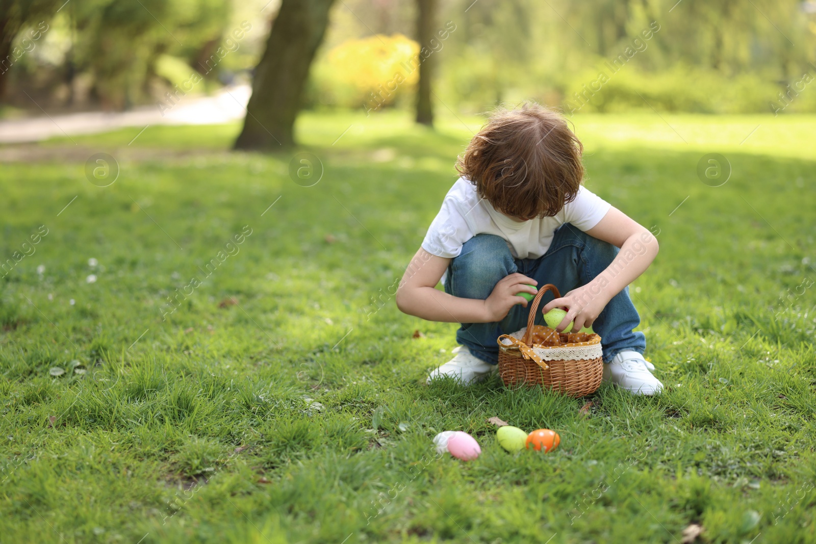 Photo of Easter celebration. Cute little boy hunting eggs outdoors, space for text