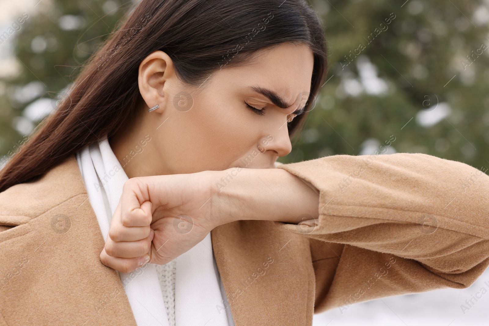 Photo of Woman in coat coughing outdoors. Cold symptoms