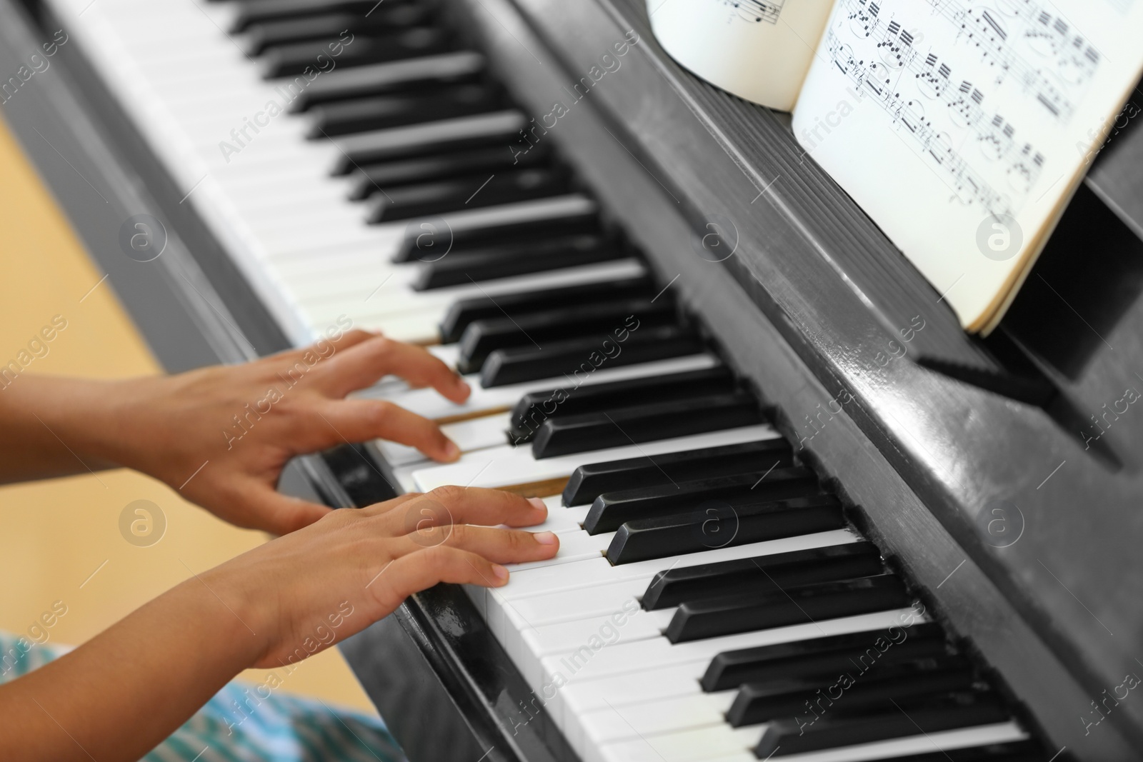 Photo of Little girl playing piano indoors, closeup. Music lesson