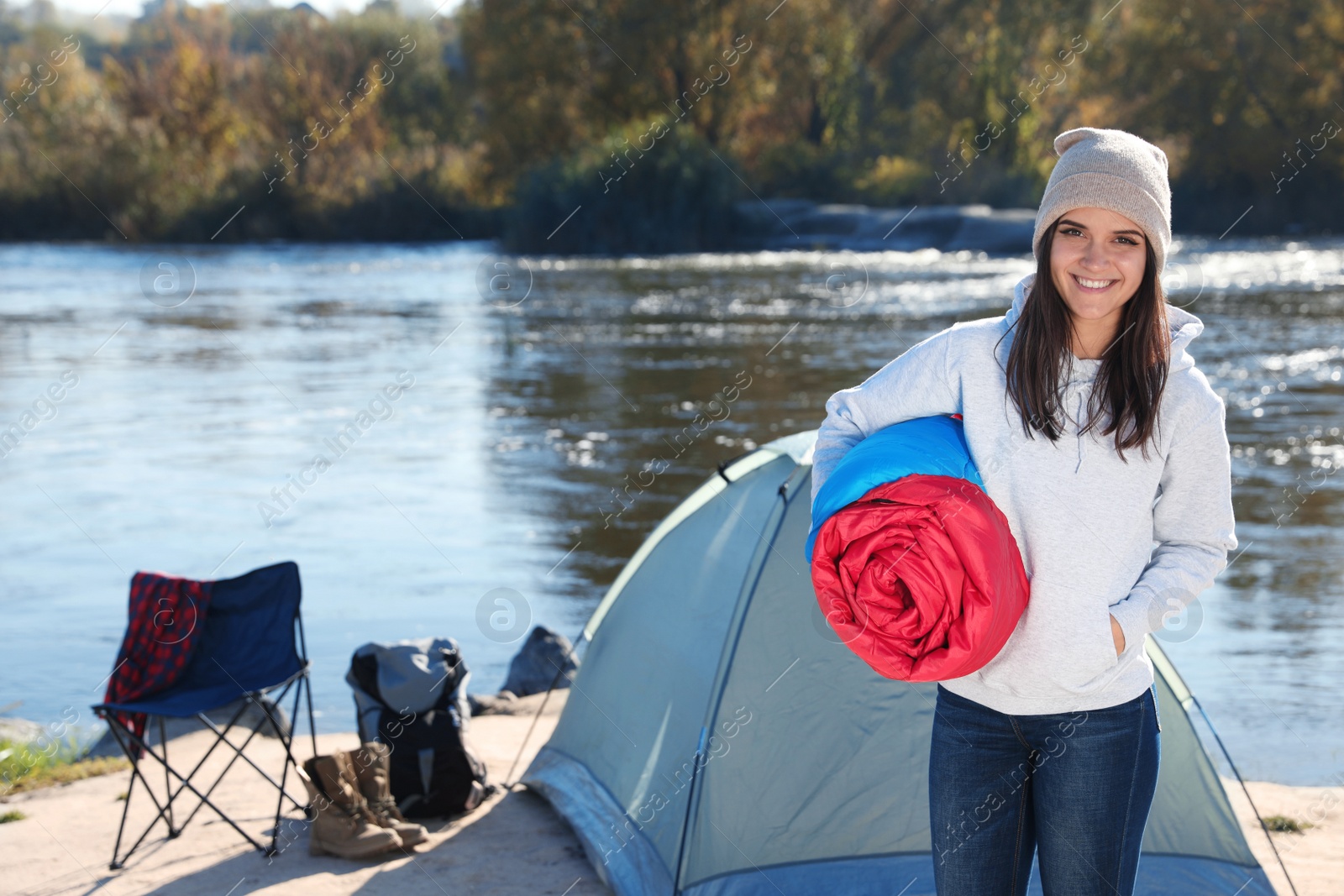 Photo of Young woman with sleeping bag near camping tent outdoors. Space for text