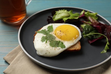 Photo of Plate with tasty fried egg, slice of bread and salad on light blue wooden table, closeup