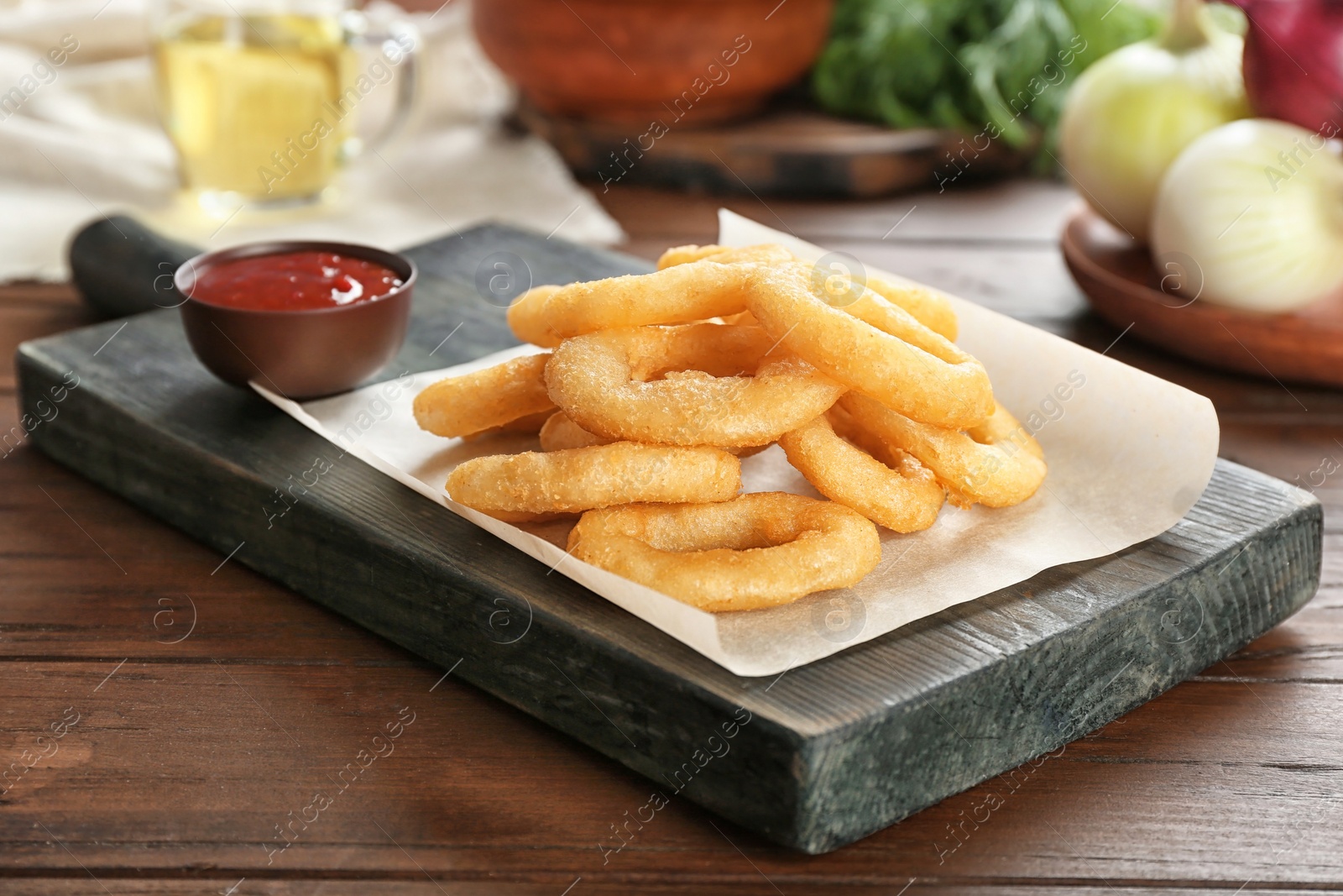 Photo of Tasty fried onion rings and bowl of ketchup on wooden table