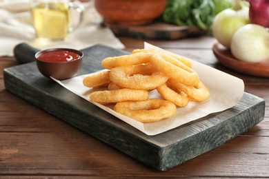 Photo of Tasty fried onion rings and bowl of ketchup on wooden table