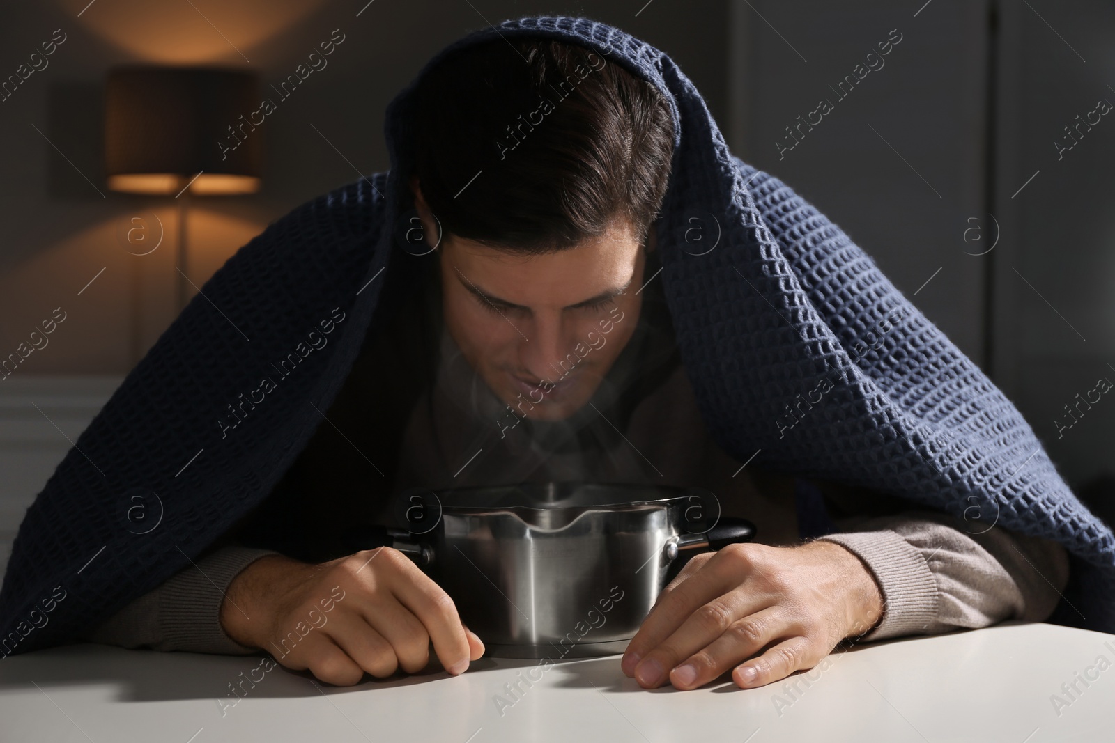 Photo of Man with plaid doing inhalation above saucepot at table indoors