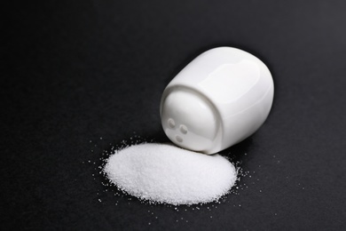 Photo of Scattered salt and shaker on black background, closeup