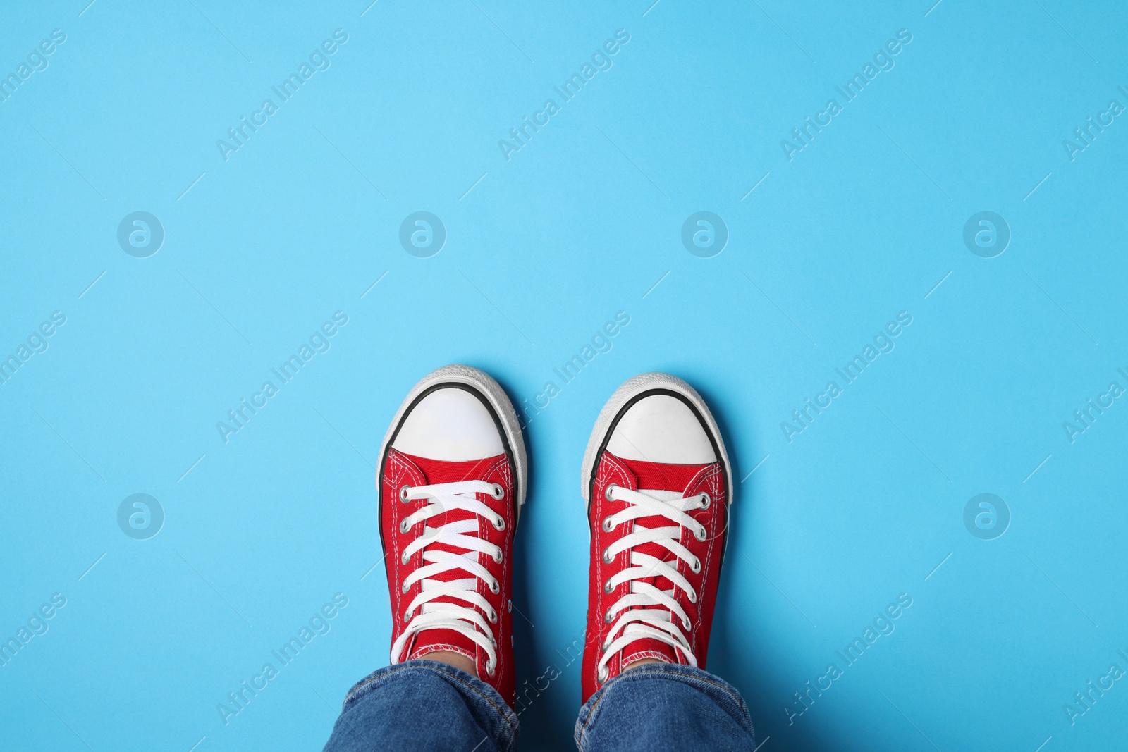 Photo of Woman in stylish gumshoes on light blue background, top view. Space for text