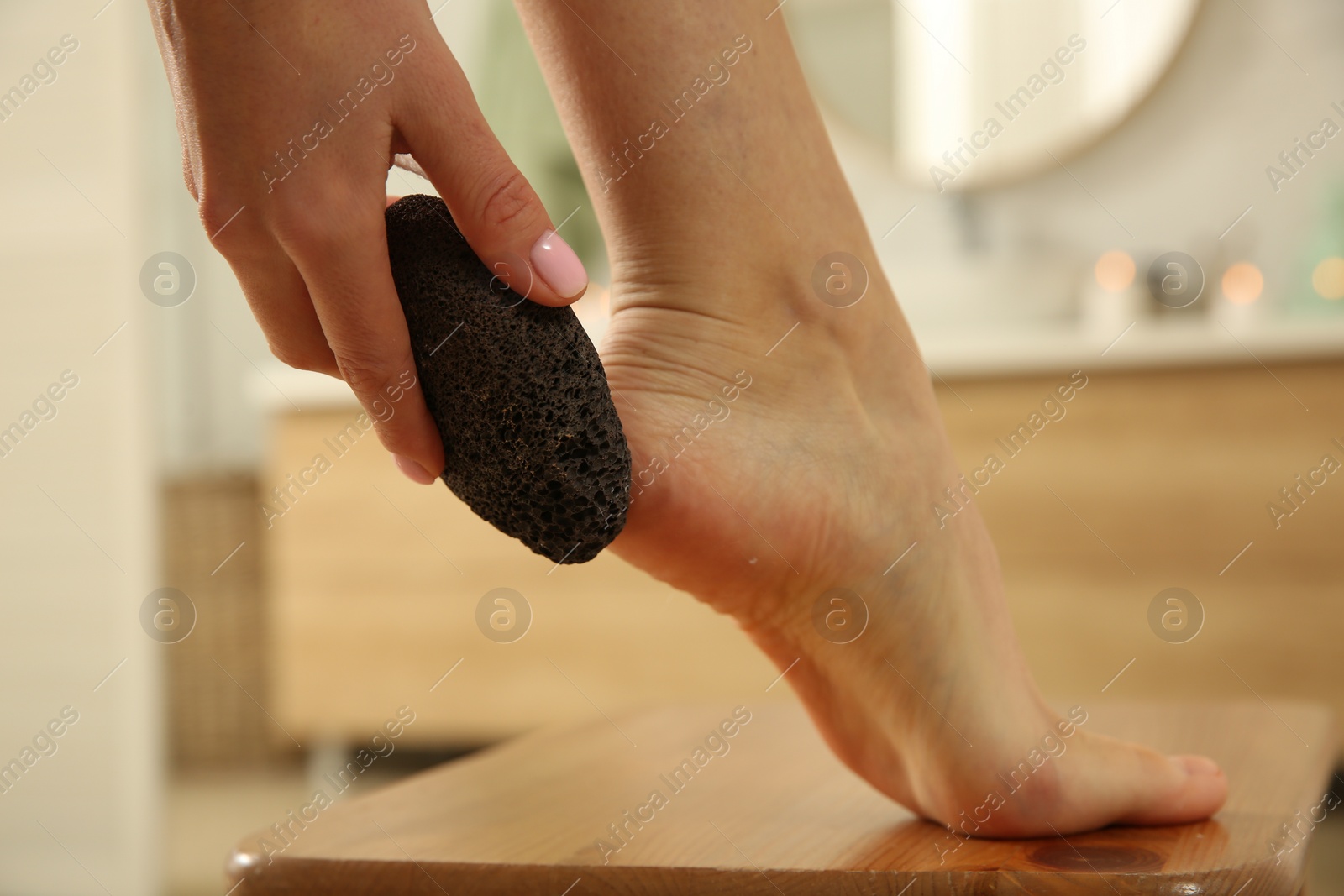 Photo of Woman using pumice stone for removing dead skin from feet in bathroom, closeup