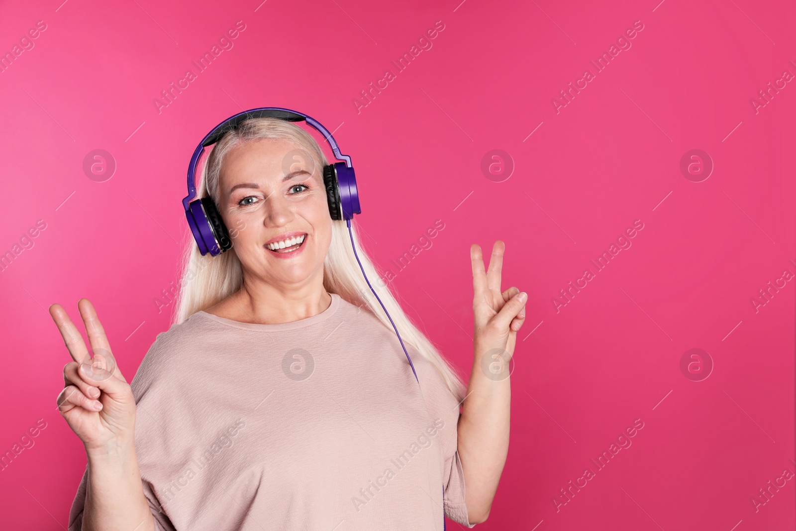 Photo of Mature woman enjoying music in headphones on color background. Space for text