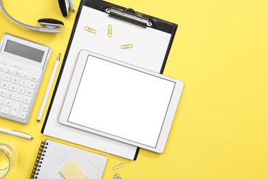 Photo of Modern tablet, stationery and headphones on yellow background, flat lay. Space for text