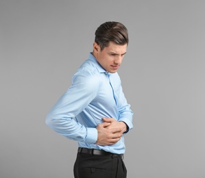 Young man suffering from flank pain on grey background