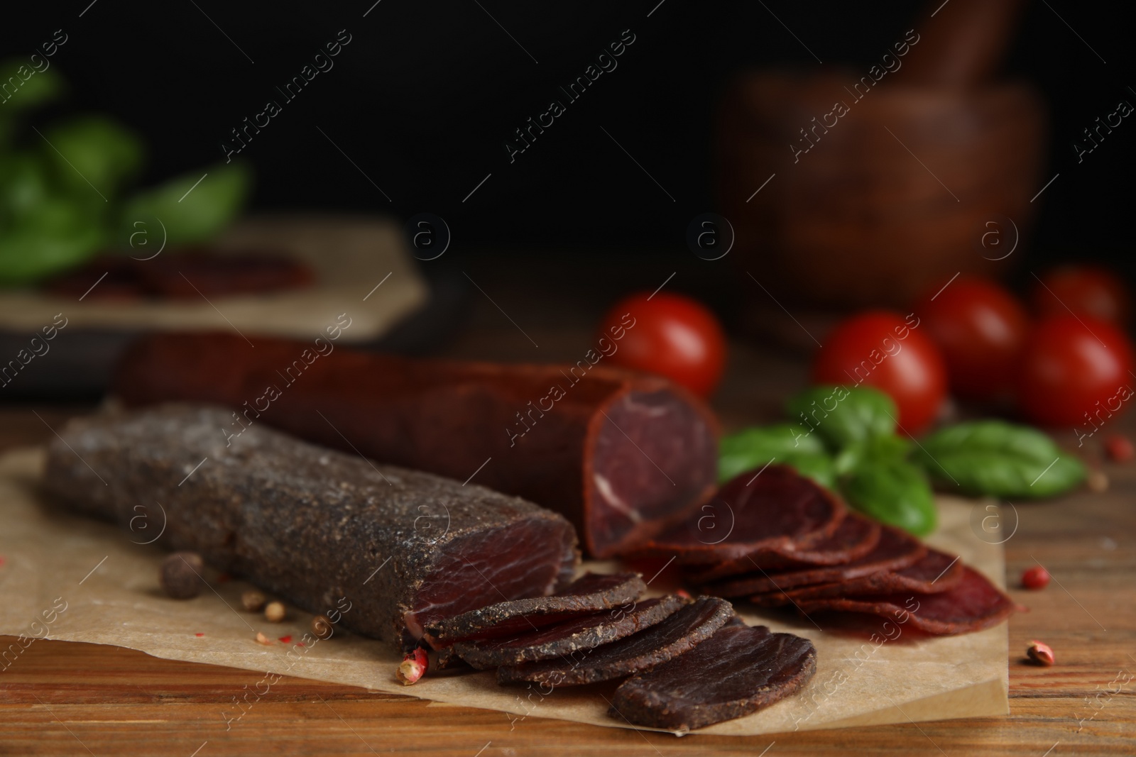 Photo of Delicious dry-cured beef basturma with basil and tomatoes on wooden table, closeup