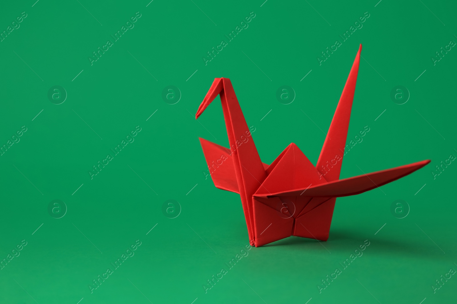 Photo of Red paper origami crane on green background, space for text